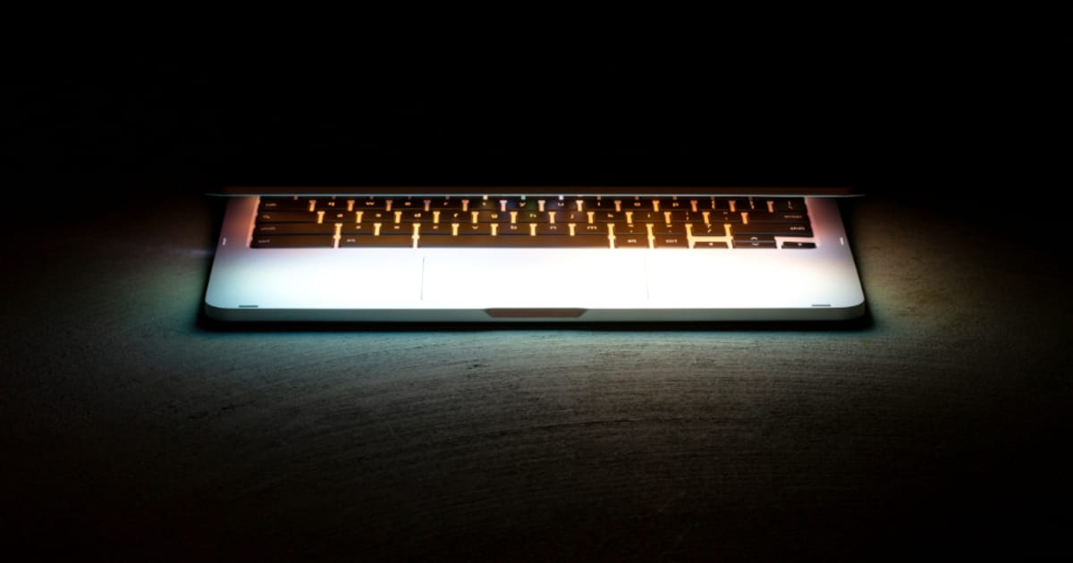 A laptop with a glowing backlit keyboard in a dark room